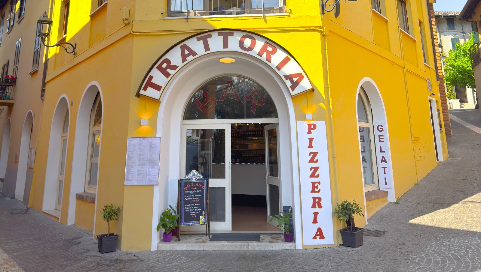 Ingresso giallo della Trattoria Adria con l'arco e le insegne Pizzeria e Gelati, Gardone Riviera